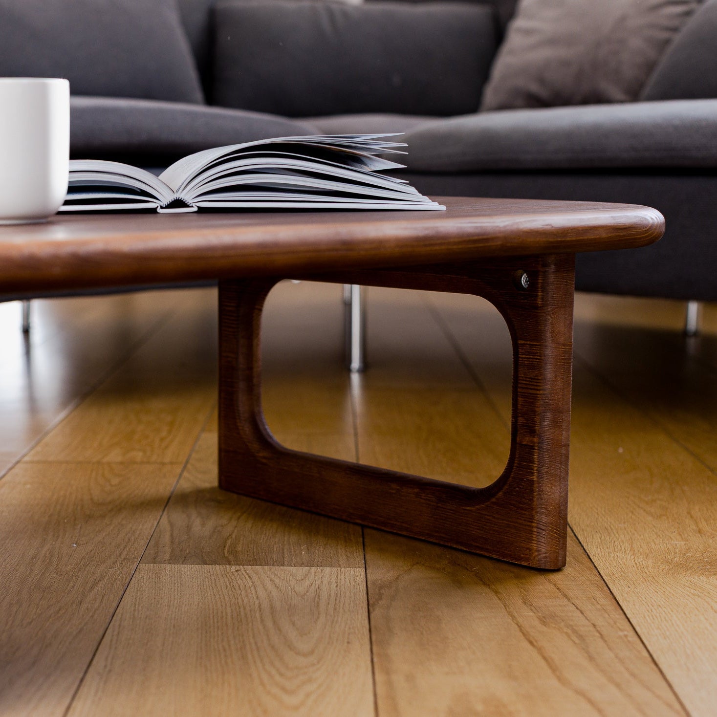 Wooden coffee table with a book and mug on a living room floor.