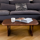 Gray sectional sofa with a wooden coffee table featuring a magazine and cup on a wooden floor.